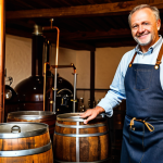 A professional, middle-aged German brewmaster, fully clothed in modest, traditional work attire including a sturdy apron and a clean shirt. He stands within a historic, small family brewery, surrounded by traditional copper brewing kettles and rustic wooden barrels. The scene is illuminated by warm, inviting light. The brewmaster gestures with one hand towards the brewing equipment, holding a small sample glass of amber beer in the other, passionately explaining the brewing process. He has an engaged, knowledgeable expression. The image conveys authenticity and deep tradition, appropriate content, safe for work, perfect anatomy, correct proportions, natural pose, well-formed hands, proper finger count, natural body proportions, professional photography, high quality, family-friendly.